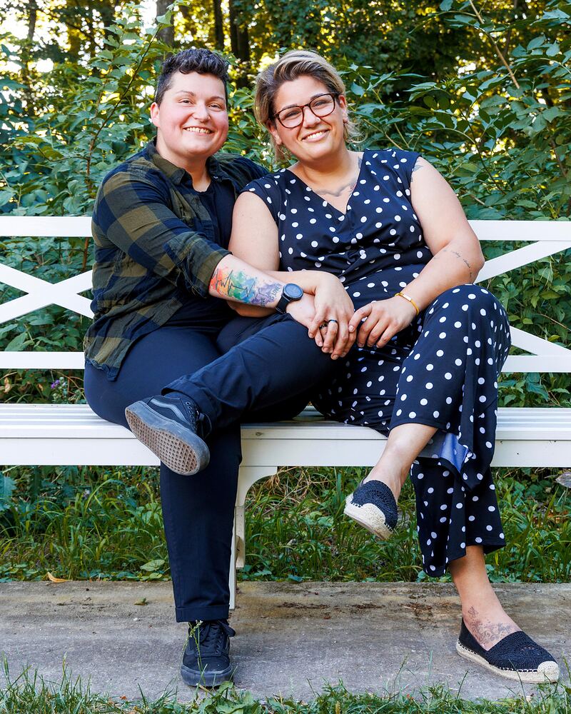 Michaela (links) und Paula (rechts) sitzen nebeneinander auf einer weißen Bank vor dichtem Grün